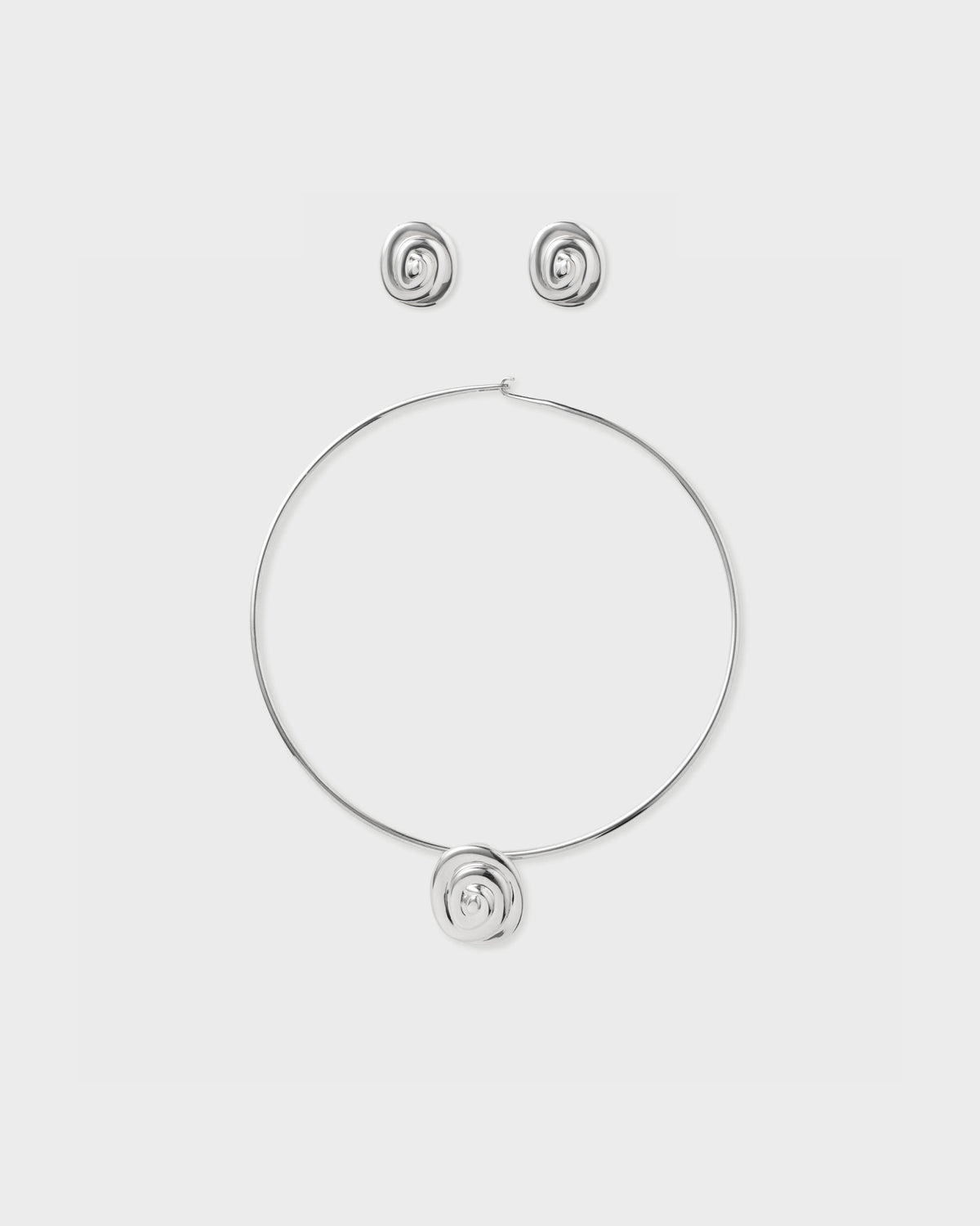 Eliou silver swirl rose earrings and matching wire choker necklace with rose pendant, flat lay on light grey