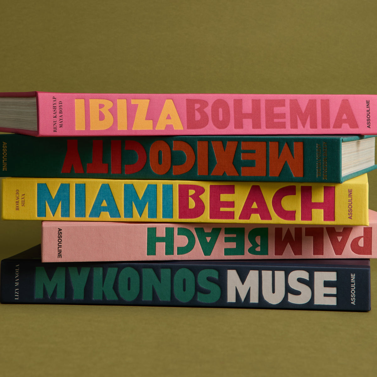 Stack of five Assouline travel coffee-table books in bright cloth spines: Ibiza Bohemia, Mexico City, Miami Beach, more