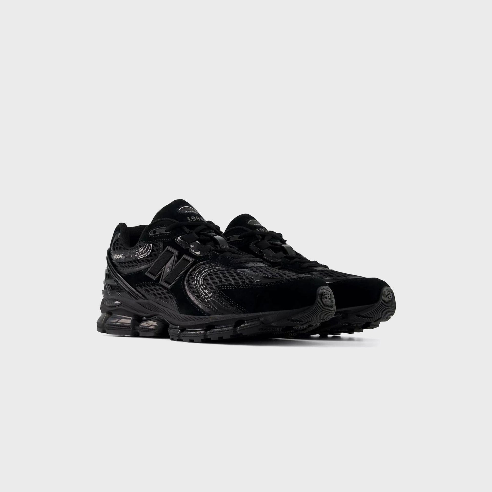 Pair of New Balance 1954R sneakers in all black with glossy overlays and mesh, front three-quarter view