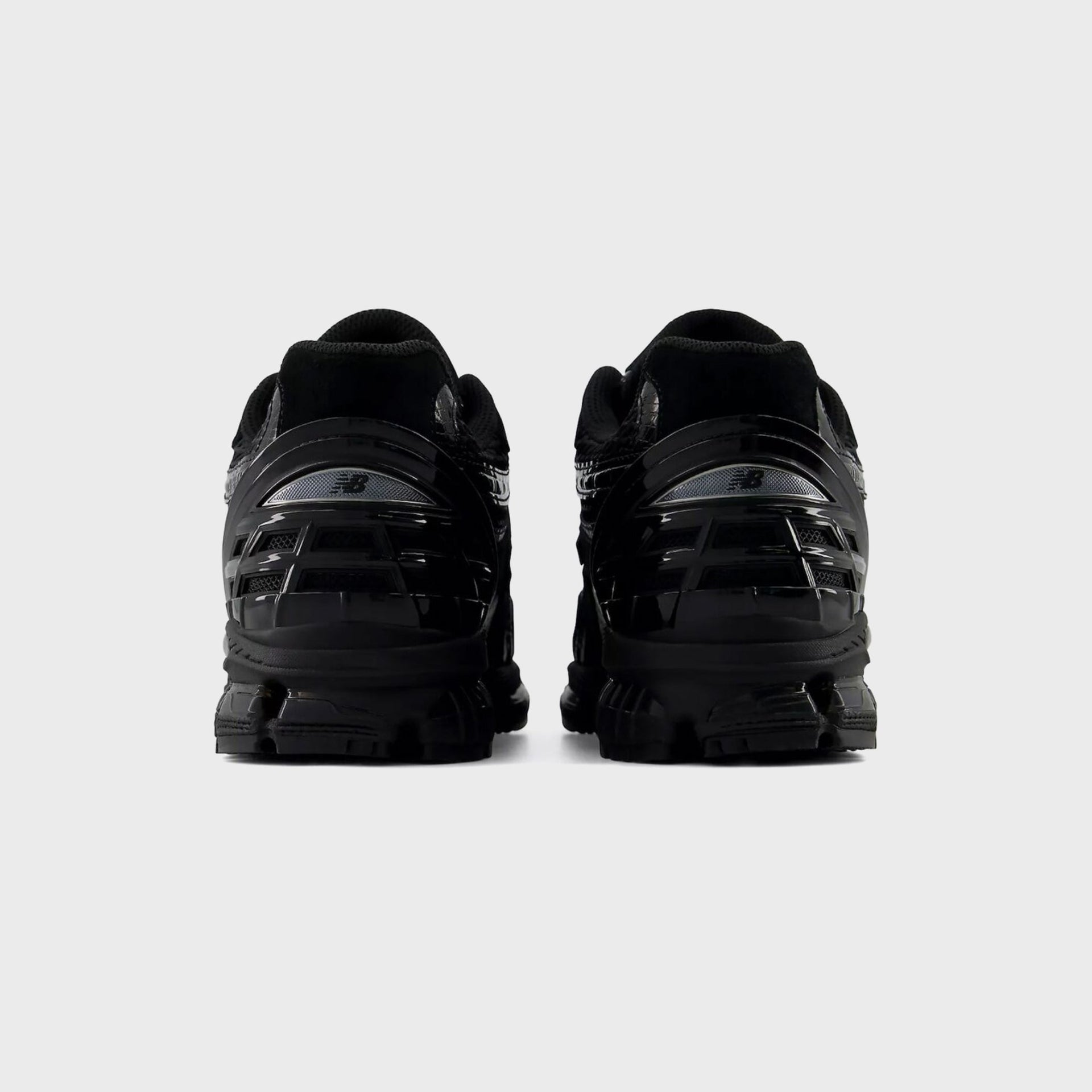 Rear heel view of a pair of New Balance 1954R Black sneakers showing the glossy caged heel counter and N logo
